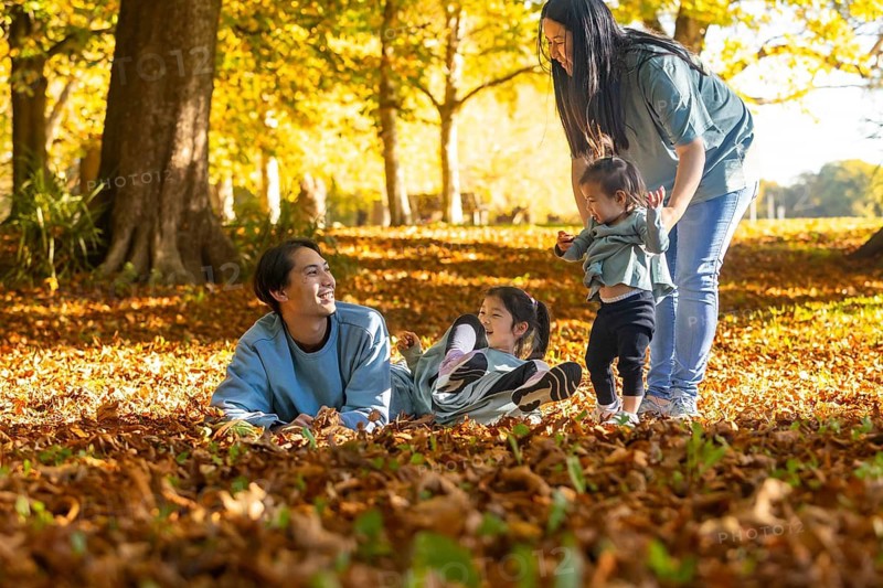 An Asian family relishes a joyful autumn day in the forest. Parents and children engage in playful moments amidst falling leaves, surrounded by trees and natural beauty