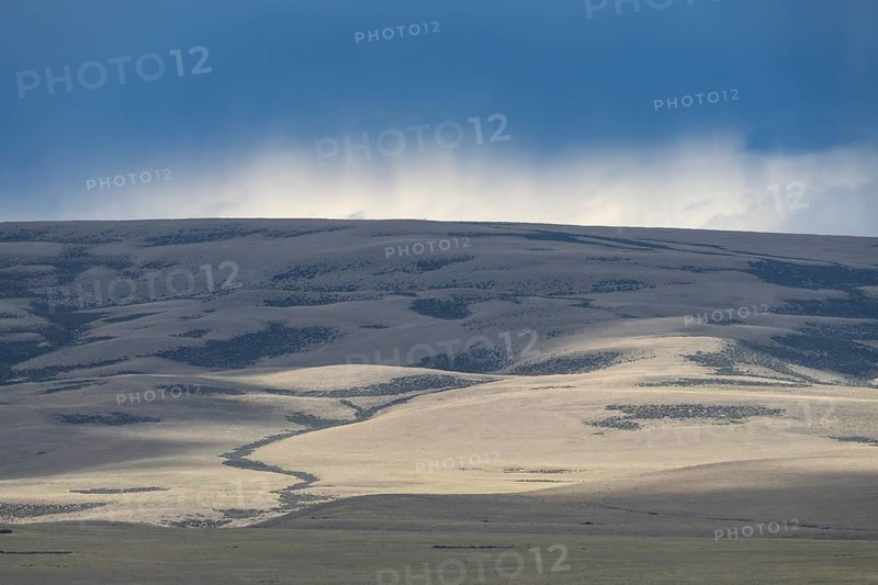 Sunlight and cloud shadows on vast steppe hills, rising rain clouds over the horizon, Patagonia, Santa Cruz province, Argentina