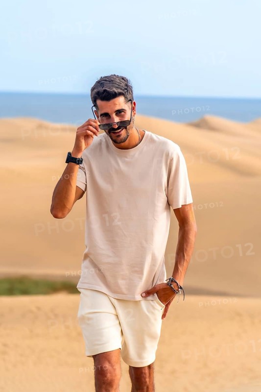 Young male tourist lowering sunglasses while walking on the maspalomas dunes in gran canaria, spain, enjoying summer vacation