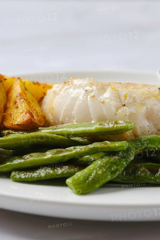 A plate showcases tender white fish alongside perfectly roasted golden potatoes and vibrant green beans. The dish highlights fresh ingredients, ideal for a nutritious and satisfying meal