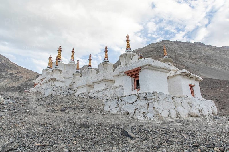 Scenic view of ancient stupas in Diskit, Nubra Valley, India, set against a dramatic Himalayan landscape. The stupas intricate details reflect Buddhist culture and history