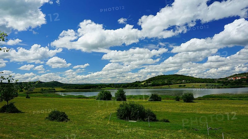 Green landscape with a lake and hills under a blue sky full of white clouds, Velence, Hungary