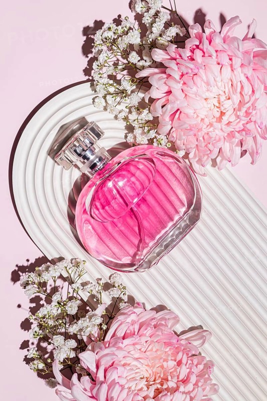 Pink perfume bottle paired with lush pink flowers on a textured white base, capturing a sense of elegance and luxury with blooming beauty and sophisticated design