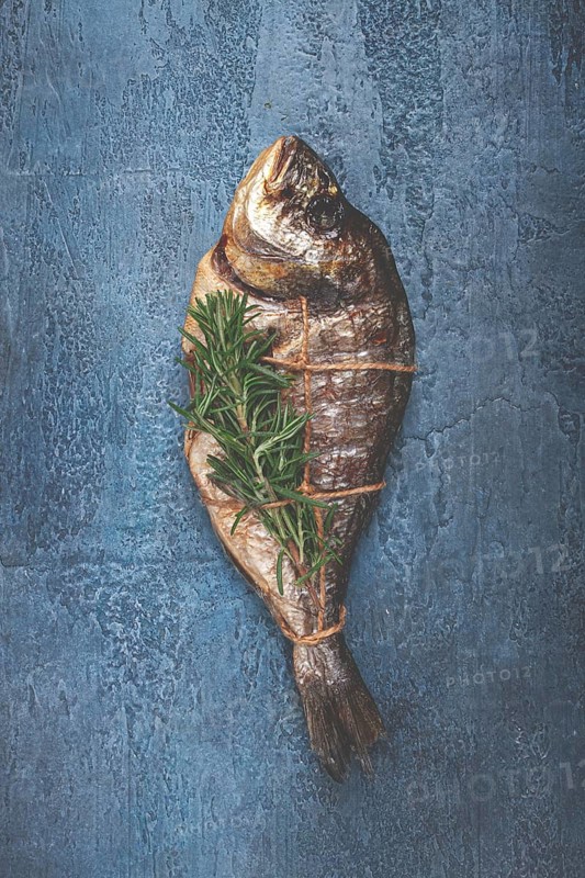 Dorado fish, hot smoked, with a sprig of rosemary, tied with a rope, on a blue background, top view, smoked fish, close-up, no people