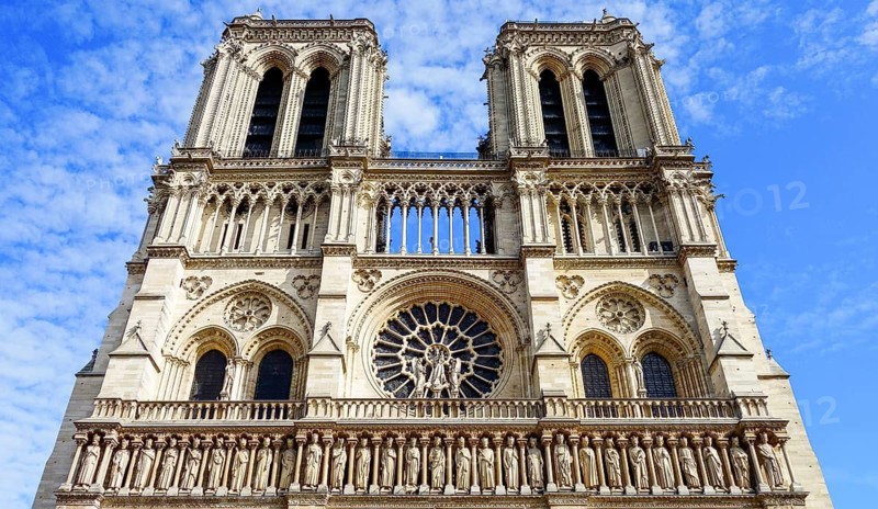 From below front view of the iconic Notre Dame Cathedral in Paris, France, showcasing its intricate Gothic architecture, twin towers, statues, and stained-glass rose window under a clear blue sky