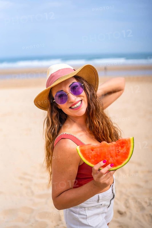 Caucasian woman enjoying summer on the beach on vacation with hat and a watermelon