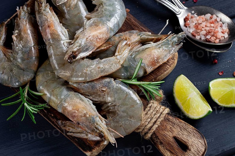 Fresh raw, white-footed shrimp, tiger prawns vannamei, on a wooden cutting board, with lime slices, and seasonings