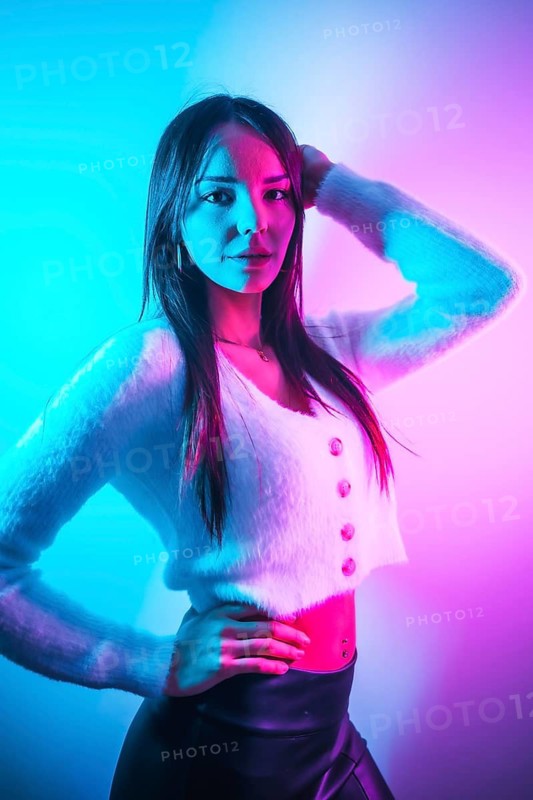 Party lifestyle in a nightclub with pink blue neon lights, a young brunette Caucasian woman in a white wool sweater, vertical photo