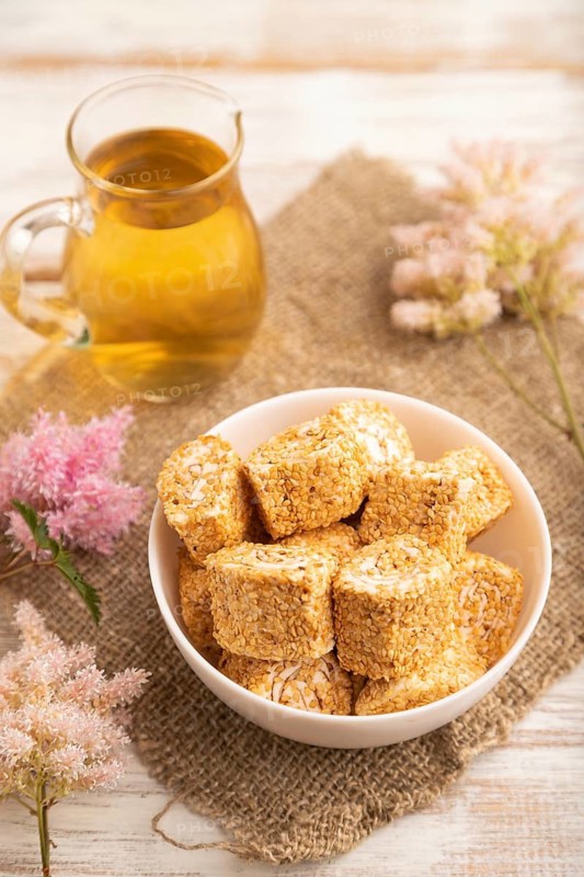 Traditional turkish delight (rahat lokum) in white ceramic plate with glass of green tea on a white wooden background. side view, close up, selective focus
