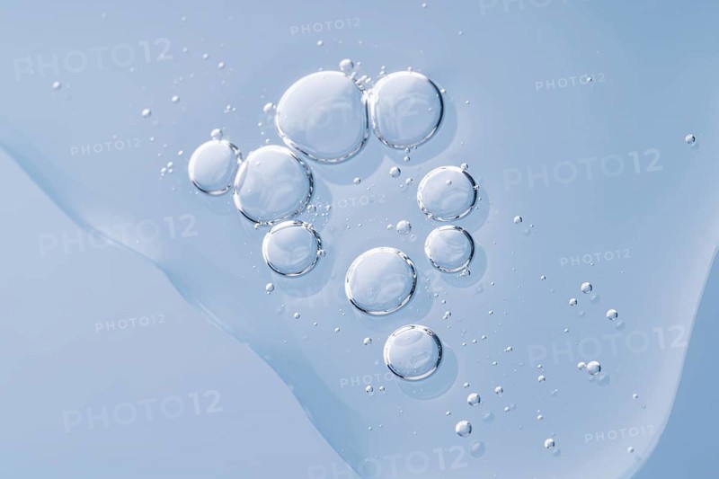 Clear, glistening serum drops elegantly arranged on a smooth, blue surface, reflecting purity and cleanliness in a tranquil setting
