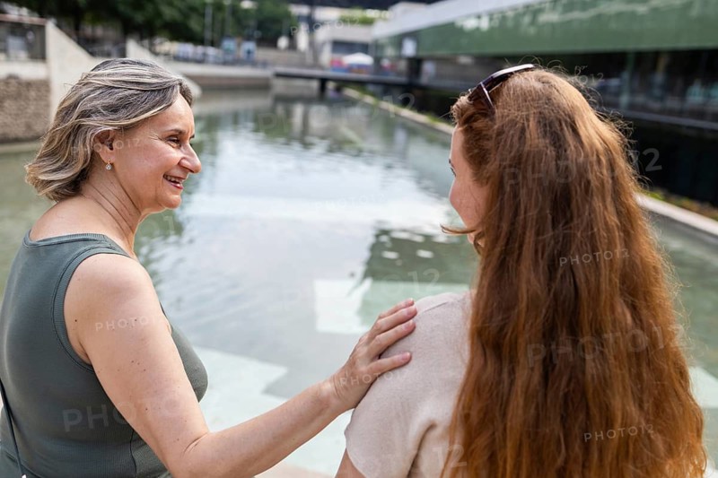 A heartfelt moment as a mother and daughter share a tender conversation by a tranquil water. A scene depicting warmth, connection, and the joy of family bonds