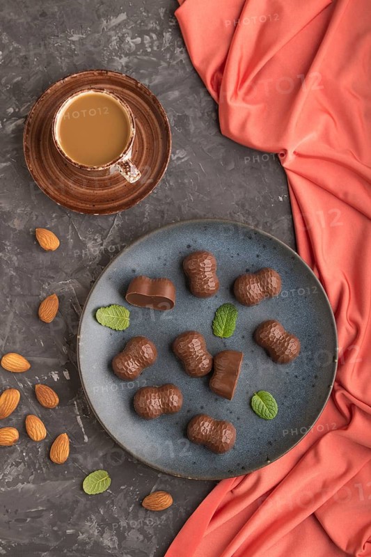 Chocolate candies with almonds and a cup of coffee on a black concrete background and red textile. top view, flat lay, close up