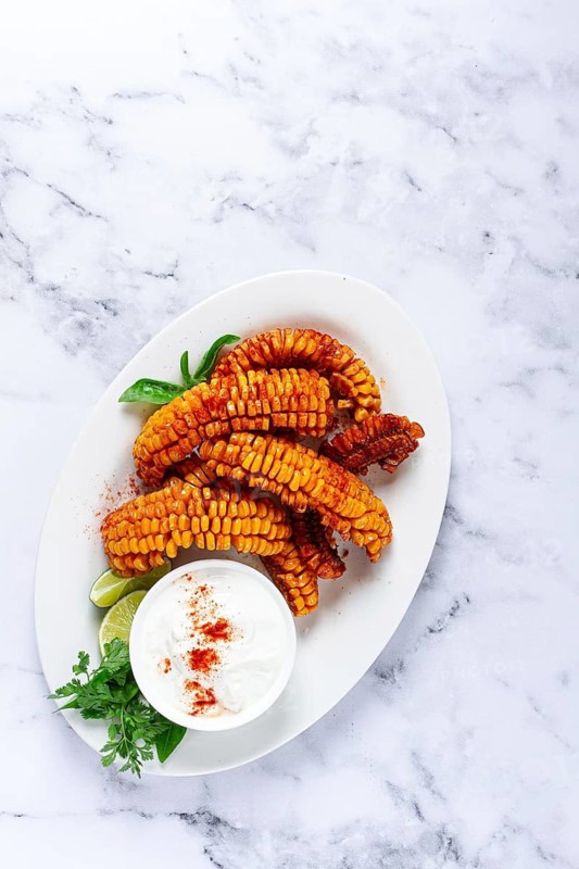 Corn ribs, with cream sauce, spices and lime, appetizer, on a white plate, homemade, no people