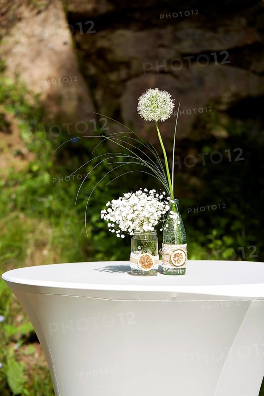 A beautifully decorated white table with glass bottles as centerpieces, filled with delicate white flowers and accented with dried lemon slices, creating a romantic, elegant atmosphere