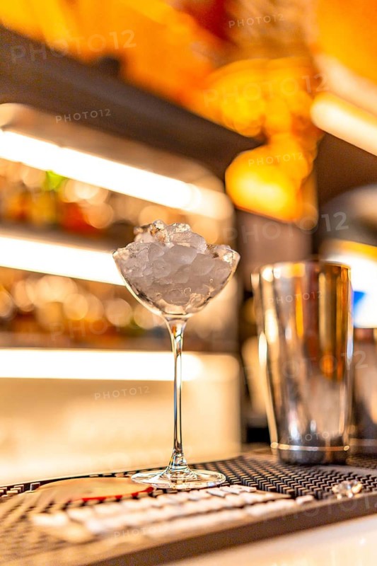 Vertical photo with no people of a luxury cocktail on a night club counter next to a shaker
