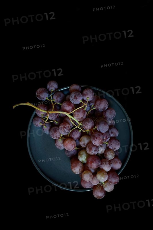 Red grape vine (Vitis vinifera) on plate against dark background