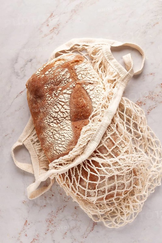 Freshly baked rye bread, ciabatta, in a mesh bag, on a marble light table, natural light