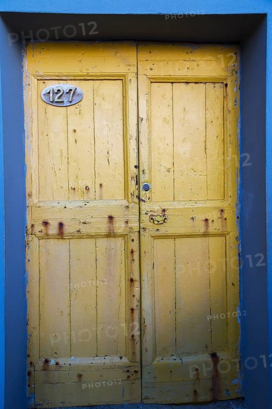 Close-up of yellow painted wood plank entrance doors on blue stucco cladded residential building facade, Riomaggiore, Cinque Terre, La Spezia province, Italy