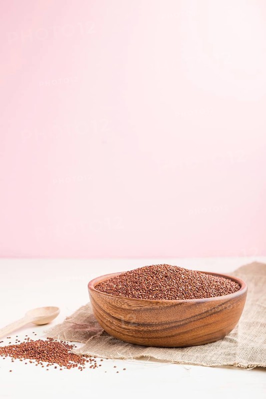 Wooden bowl with raw red quinoa seeds on a white and pink background and linen textile. Side view, copy space, selective focus