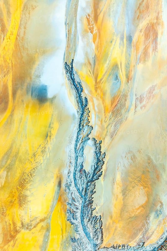 A mesmerizing aerial view capturing intricate fractal patterns in mud, highlighted with vivid blue and yellow hues. The abstract design evokes a sense of natural artistry