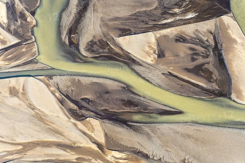 This stunning aerial photograph captures sinuous golden-tinted rivers flowing through a contrasting landscape of black sand in Iceland, showcasing nature's artistry from an elevated perspective