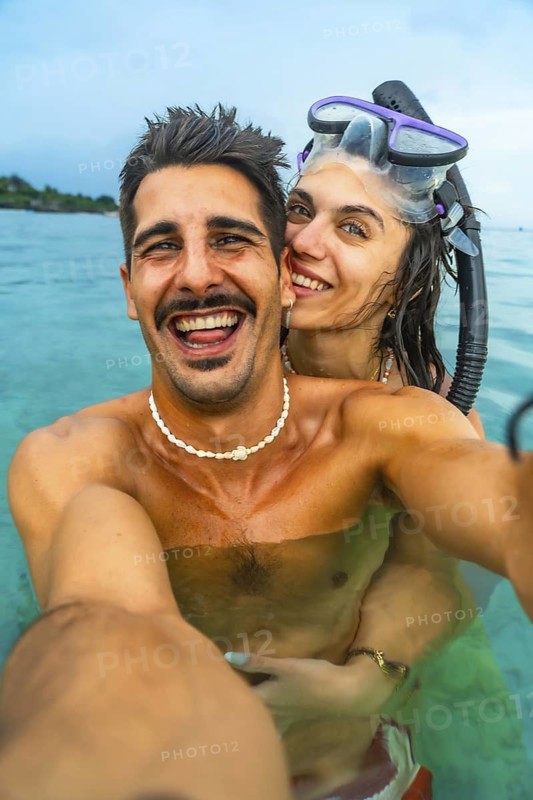 Young couple having fun taking a selfie while snorkeling in the ocean on a beautiful tropical island