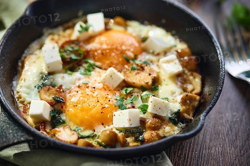 Fried eggs with spinach, mushrooms, grated cheese and feta cheese in small cast iron skillet, close up