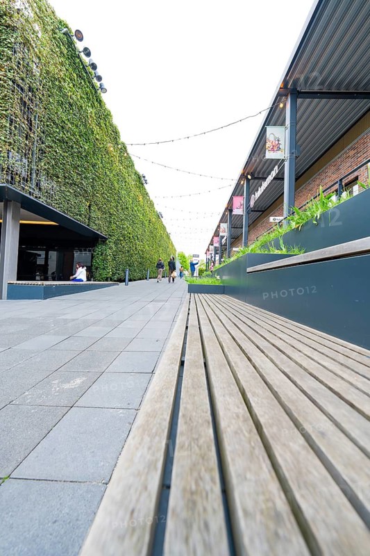 Long path with wooden bench next to a green wall in a modern urban area, Outlet City Metzingen, Germany