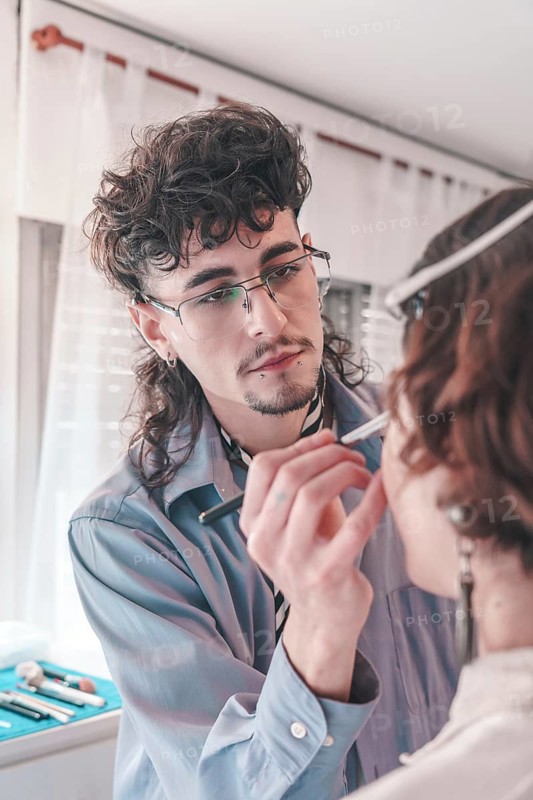 Professional makeup artist carefully applying makeup on a model's face using a brush, showcasing diversity and inclusion in the beauty industry, creating a glamorous look in a salon setting