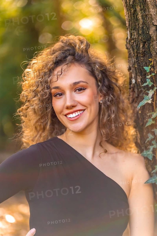 Vertical photo of a smiling woman looking at camera standing in the forest