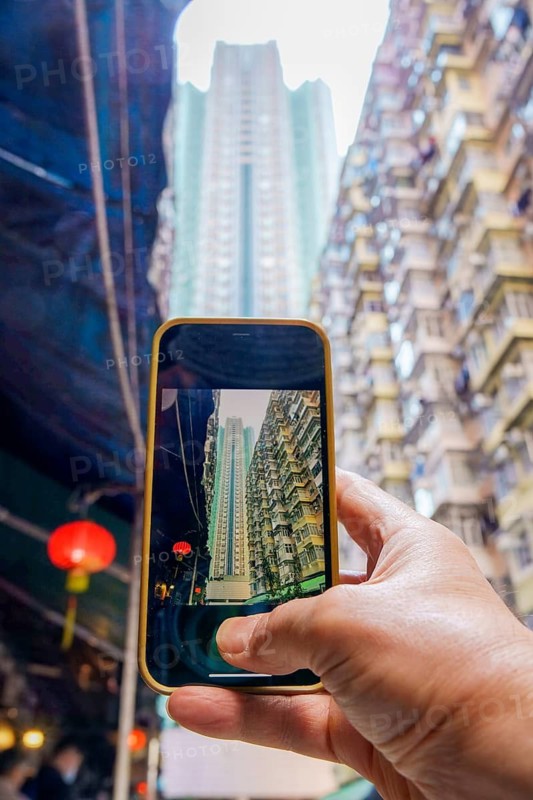 Cropped unrecognizable hand holding a smartphone capturing Hong Kong's towering buildings, showcasing urban landscapes and traditional decorations