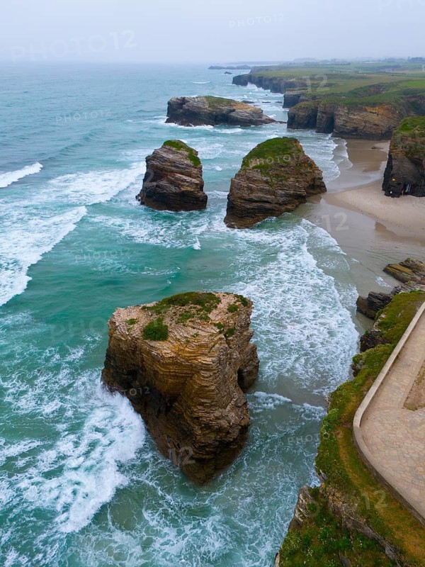 Waves crashing against large, grass-covered rocks along a steep, rugged coastline, aerial view, Praia das Catedrais, Playa de las Catedrales, Cathedral Beach, As Catedrais Beach, Cantabrian Sea, Ribadeo, Galicia, Galicia, Spain