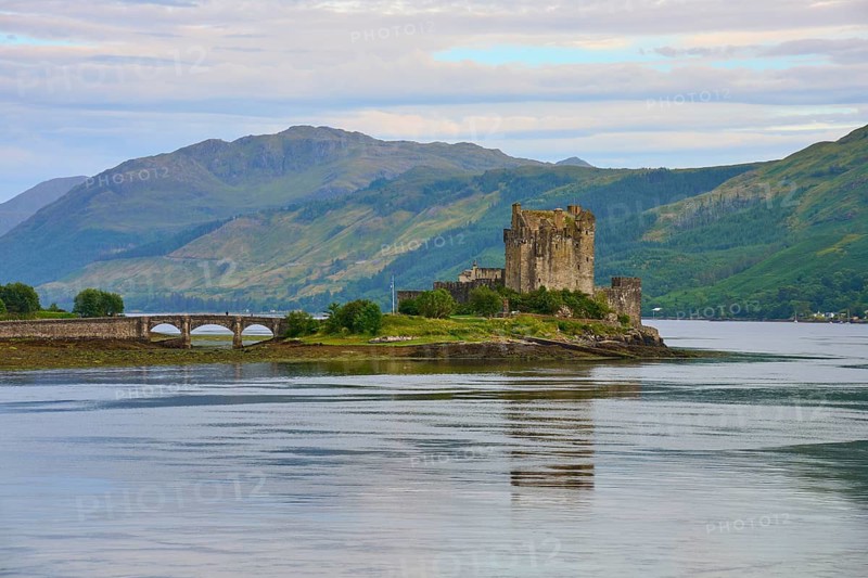 An old castle stands majestically on an island surrounded by water and green mountains under a cloudy sky, Eilean Donan Castle, Dornie, Kyle of Lochalsh, Scotland, United Kingdom, Great Britain