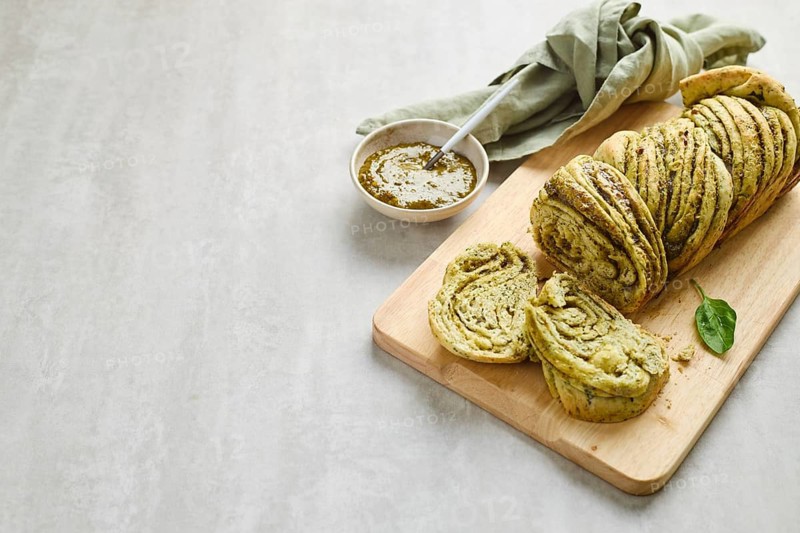 Baked homemade savoury babka plaited bread loaf flavoured with pesto on wooden bread board
