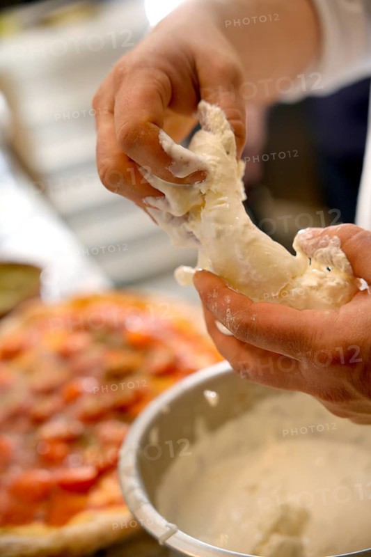 Cropped unrecognizable person preparing pizza dough with visible raw ingredients and tools in a pizzeria kitchen