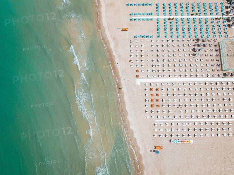 Aerial view of a beach in San Beneddetto, Italy. Rows of colorful umbrellas and lounge chairs line the sandy shore, with the turquoise sea gently lapping the coast
