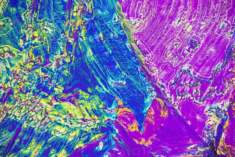 A stunning microscopic view of microcrystals showcasing a vivid array of colors including blue, green, yellow, and purple. The intricate textures and patterns reveal the beauty of scientific imaging