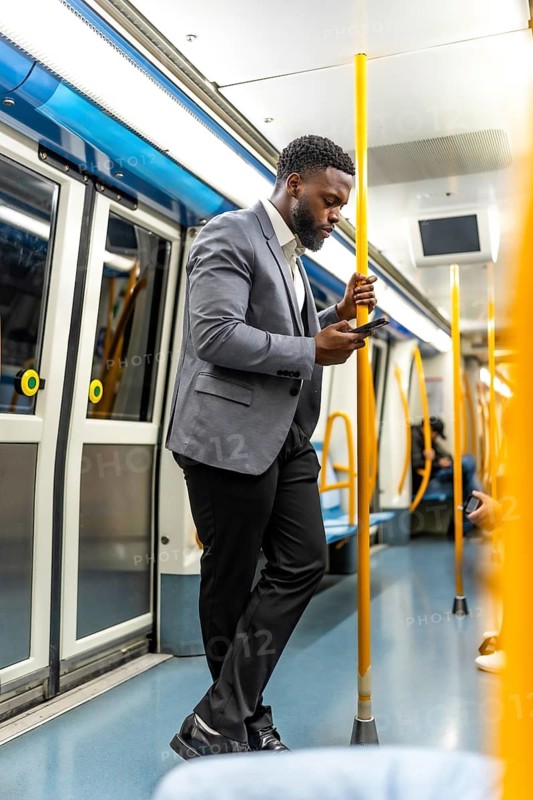 Stylish businessman using mobile phone while standing on a modern subway train, commuting to work in urban environment