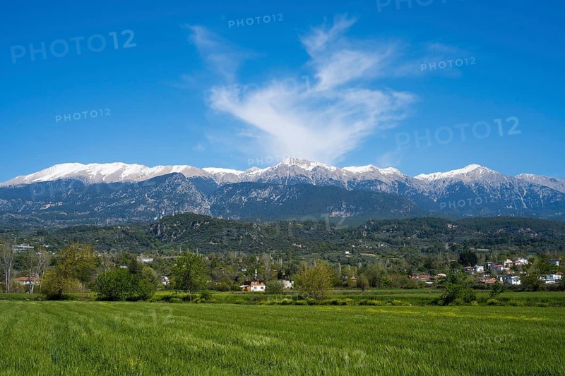 View of snowy mountains and a small village in the foreground under blue sky with clouds, landscape near Kadiköy, Mugla, Aegean Sea, Turkey