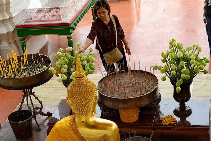 Bangkok, Thailand. February 20th 2025. A Thai visitor lights a candle and makes an offering of a white lotus flower at The Wat Suthat Thepwararam Temple, Bangkok