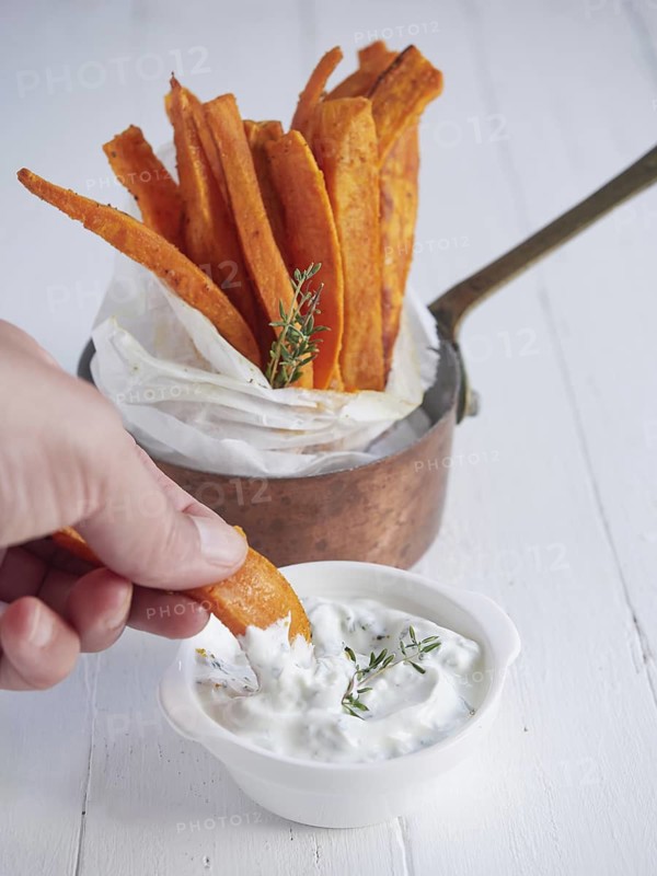 Hand dipping roasted sweet potato sticks in yoghurt sauce