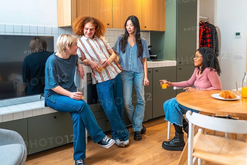 Four roommates are enjoying a casual conversation in their modern kitchen, drinking juice and eating breakfast