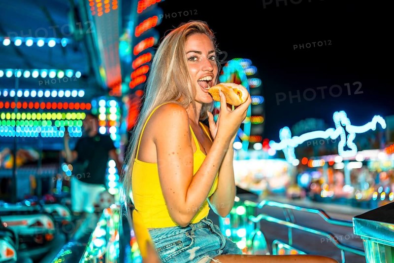 Sensual blonde woman biting into a hot dog at night fair