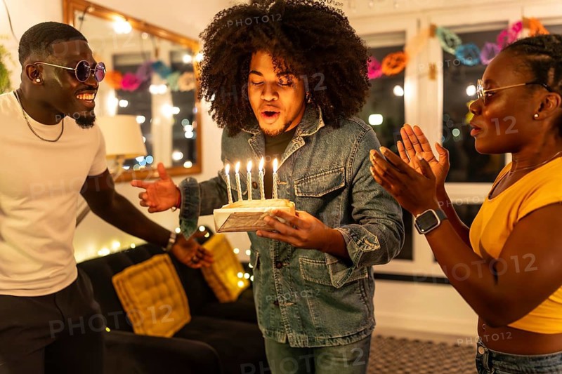 Man blowing birthday cake asking for wish next to multi-ethnic friends at home party
