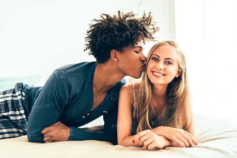 A loving couple shares a tender moment as one partner kisses the other's cheek. Both radiate happiness and warmth, capturing the essence of affection and joy in a relaxed setting