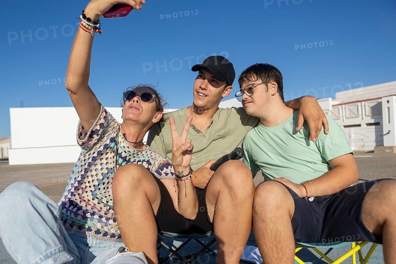 A Down syndrome teenager sits with family members outdoors, laughing and taking a selfie The scene captures the joy of spending time together and enjoying sports activities