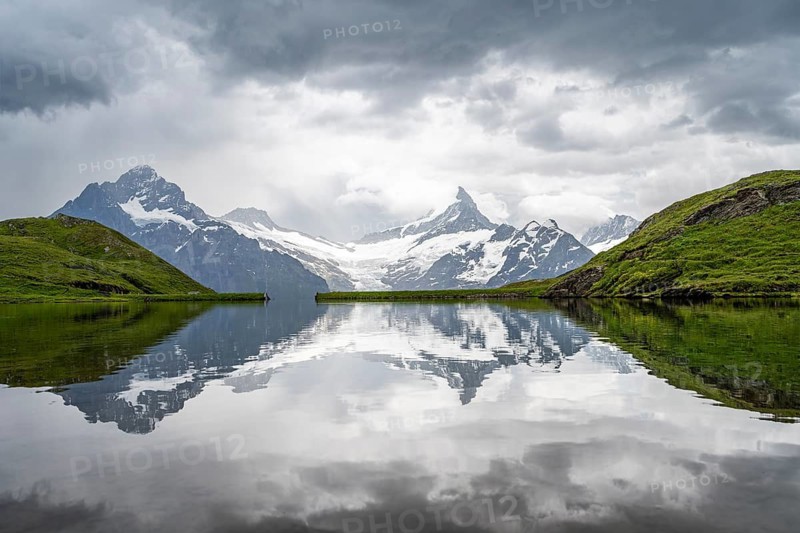 Mittelhorn and Schreckhorn peaks with Upper Grindelwald glacier are reflected in the Bachalpsee mountain lake, dramatic cloudy sky, Bernese Alps, Bernese Oberland, Switzerland