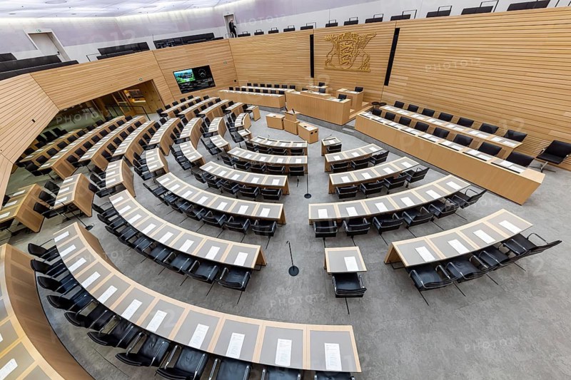 Plenary hall deserted with the seats of deputies and the government bank. Behind it is the coat of arms of the federal state. The state parliament of Baden-Württemberg is the state parliament based in Stuttgart, Baden-Württemberg, Germany