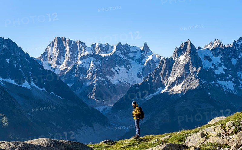 Young man in front of impressive mountain landscape in morning light, picturesque mountain landscape with imposing mountain peaks and glaciers, Mer de Glace glacier, Grandes Jorasses in the background, Mont Blanc Massif, Chamonix-Mont-Blanc, Haute-Savoie, France