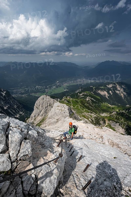 Mountaineer with helmet climbing on the rock in a secured climb, on a narrow rocky ridge, in steep rocky mountain landscape, view of Garmisch Partenkirchen, descent from the Alpsitze via the via ferrata, Alpspitz Ferrata, Wetterstein range, Bavaria, Germany